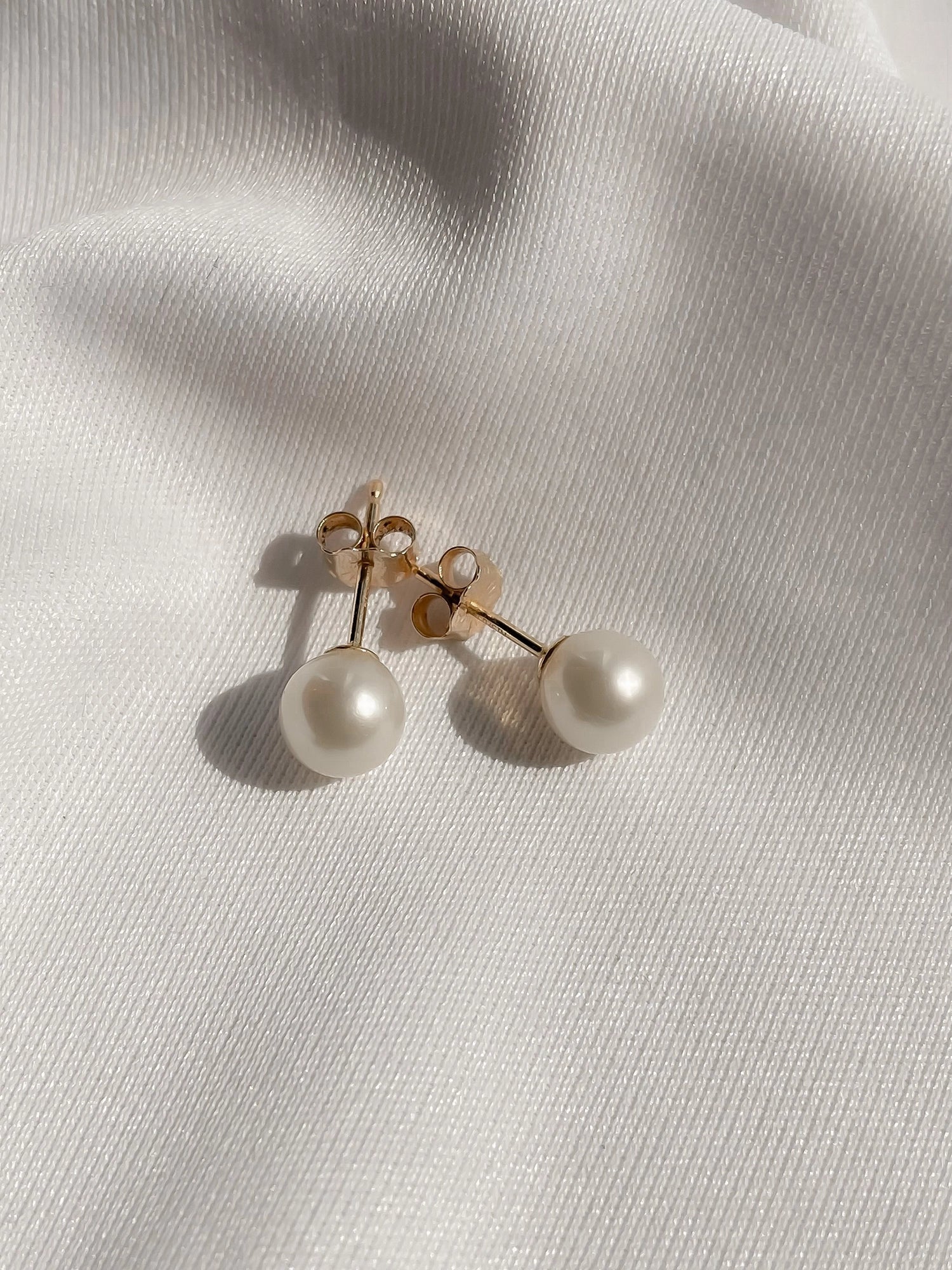 14kt Gold Mini Studs - 6-7mm white freshwater pearl earrings in 14kt yellow gold by Nishi Pearls, styled lifestyle photo